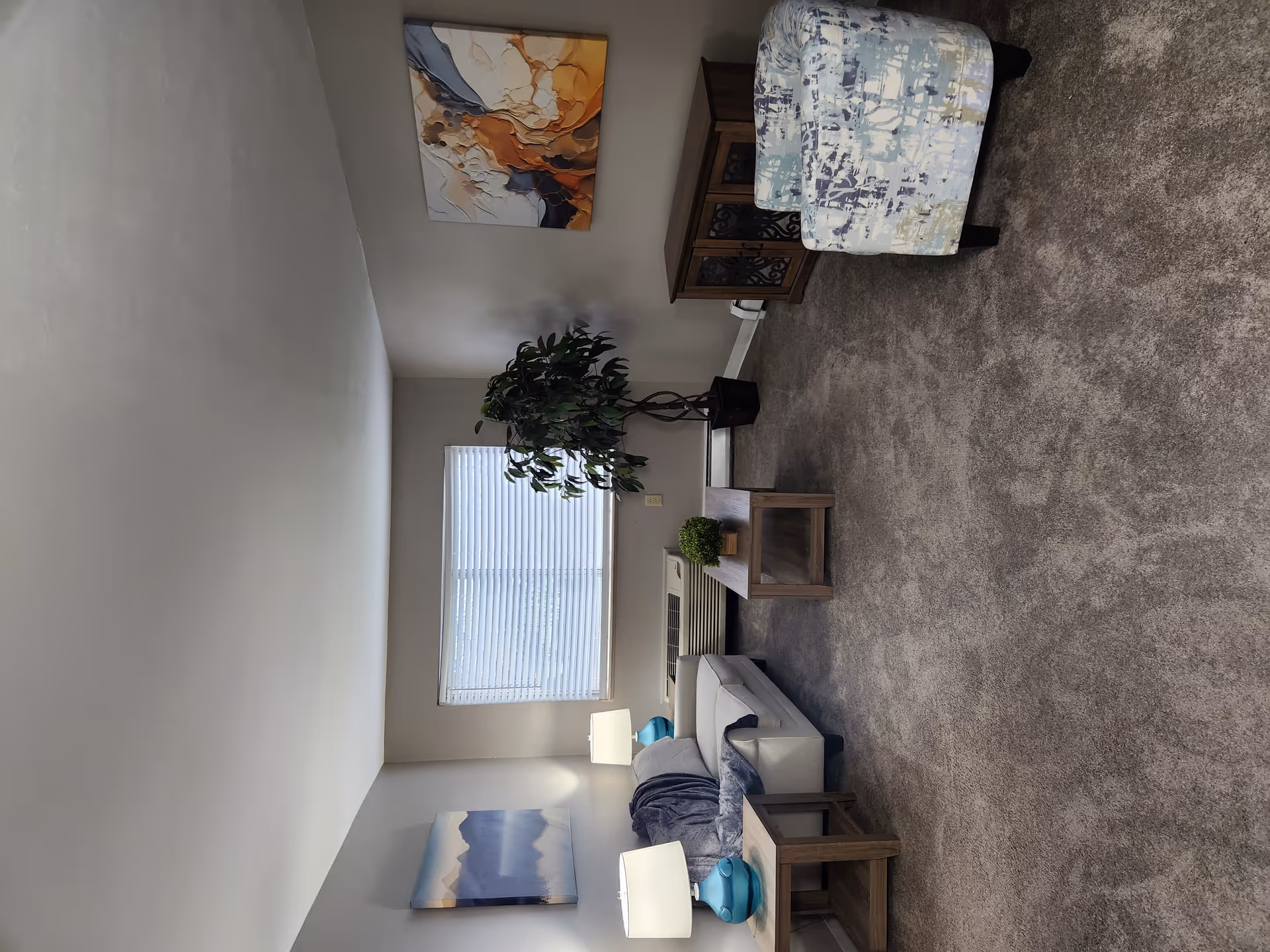 Cozy interior living room with seating, tables, plants, artwork, and a windowed view.