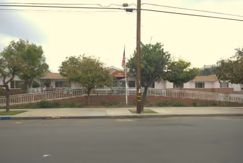 Exterior view of Glen Park at Glendale Mariposa with trees, railing, and flag.