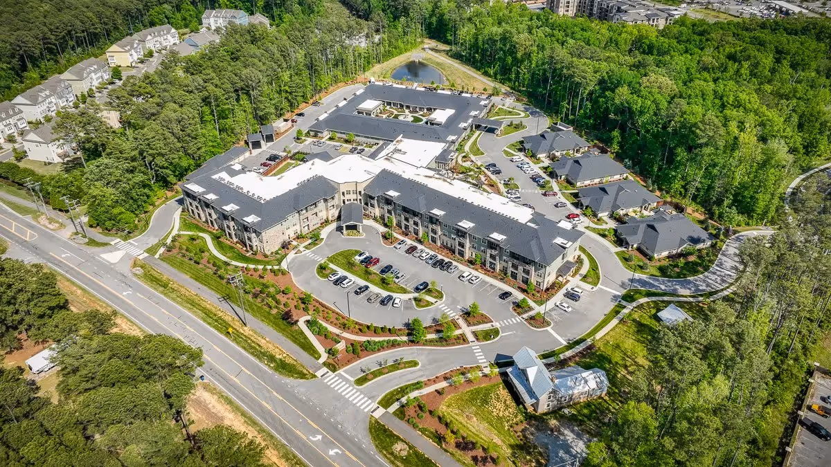 Aerial view of The Reserve at Mills Farm showing a large multi-wing senior living building, parking areas, and surrounding trees.
