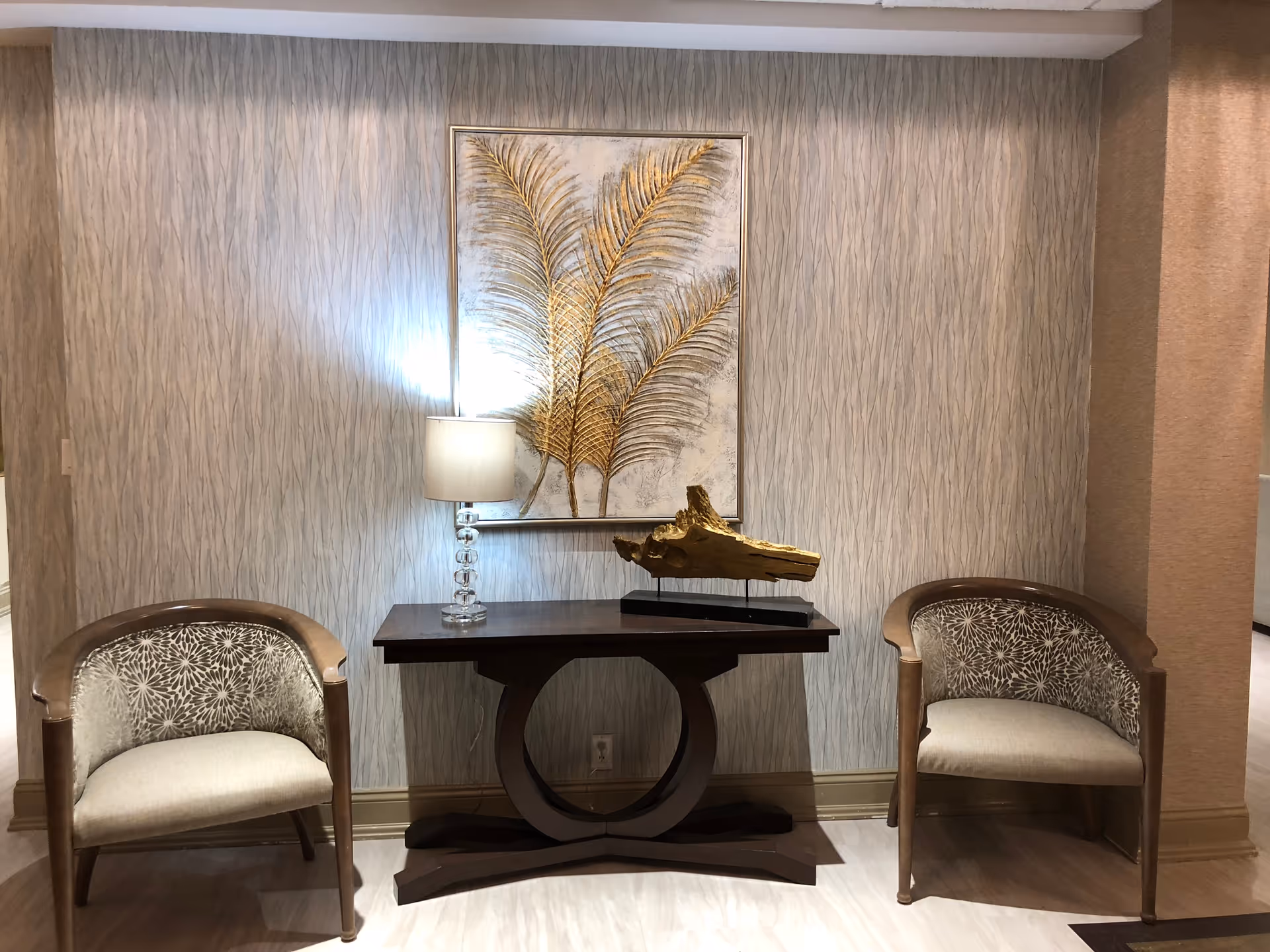 Two upholstered chairs flank a dark console table with lamp and framed artwork.