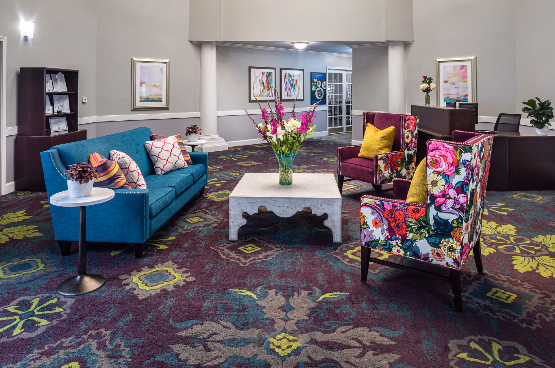 Brightly furnished lobby seating area with a teal sofa, floral armchairs and a coffee table topped with flowers.