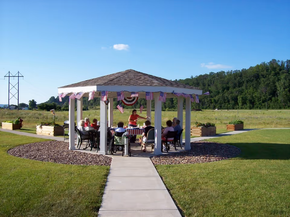 A gazebo decorated with American flags where a group of people sit at tables in a grassy outdoor area.