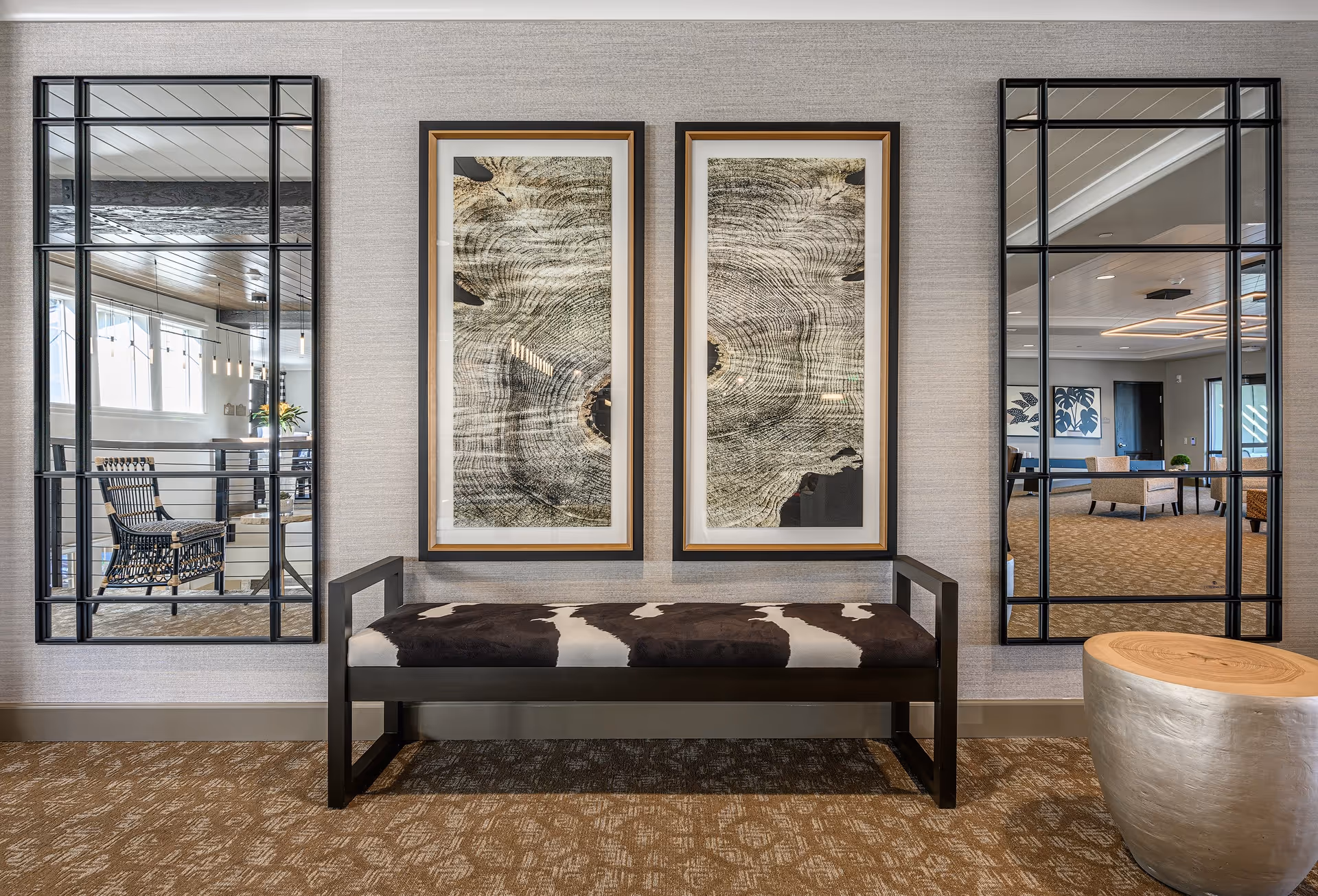 Entry seating area featuring a cowhide bench between two framed abstract artworks and tall paneled mirrors reflecting a lounge.