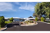 Front exterior of a single-story nursing center with a circular driveway, landscaped island, and clear blue sky.