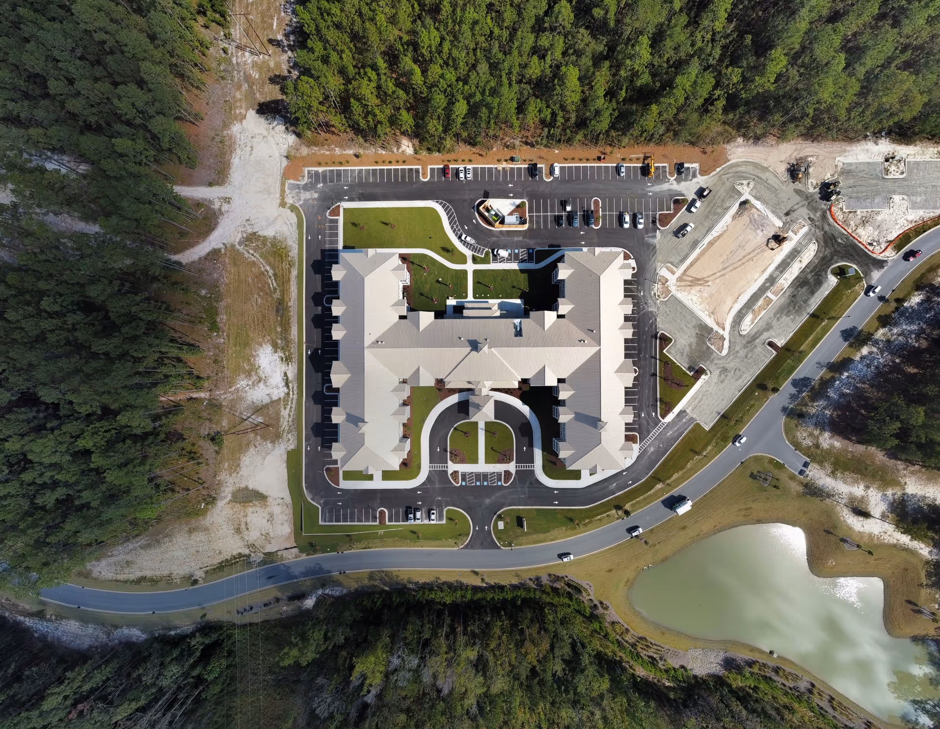 Aerial view of Arbor Landing at Compass Pointe facility showing a large building with a U-shaped layout surrounded by parking lots, roads, a small pond, and wooded areas.