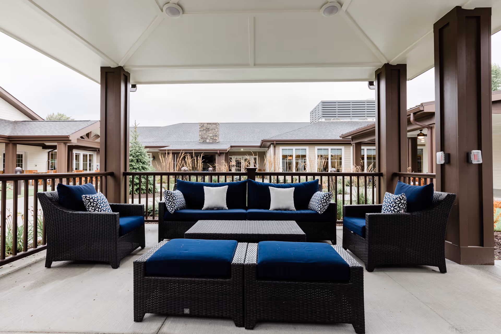 Covered outdoor patio with wicker lounge furniture and blue cushions overlooking the facility courtyard.