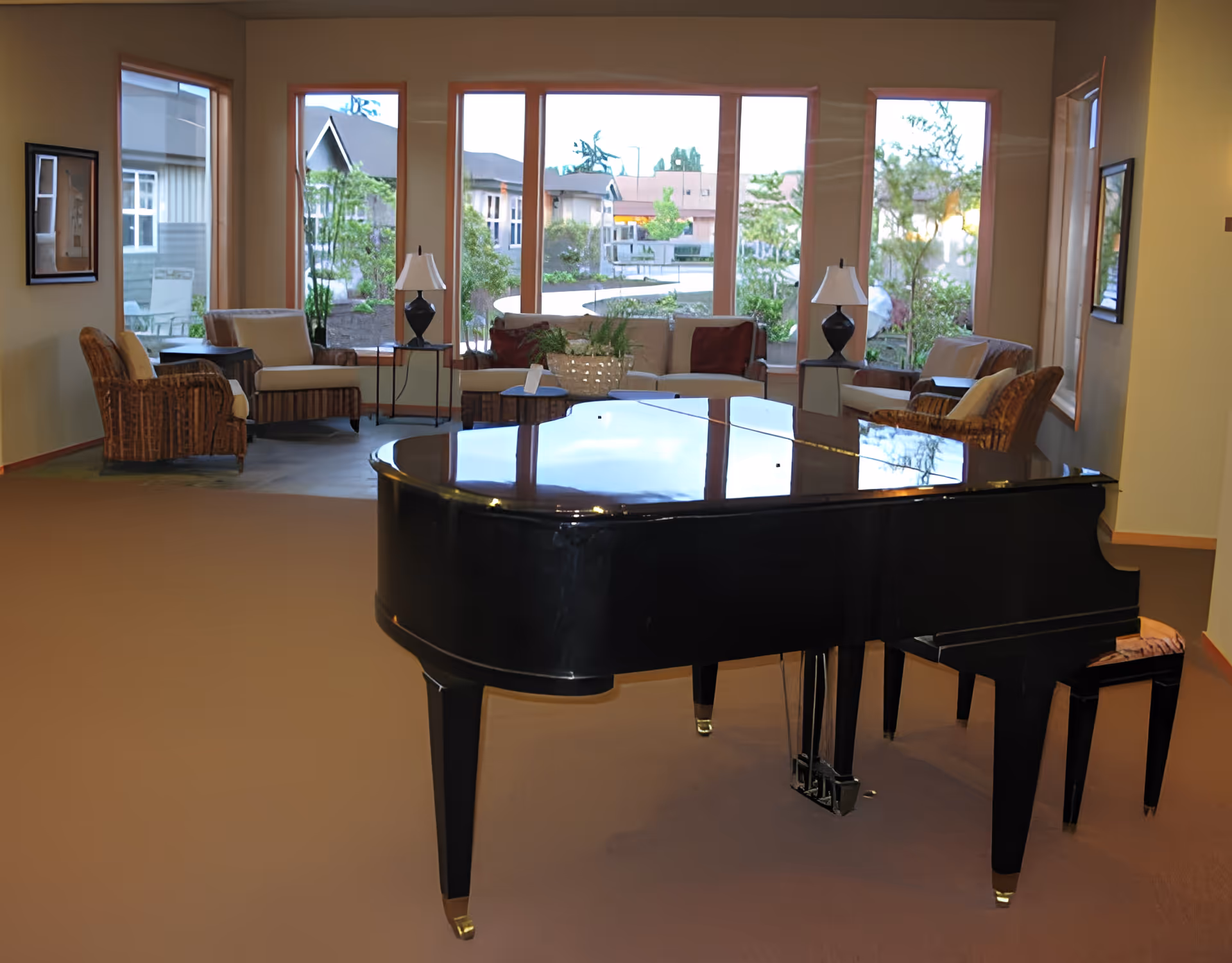 Black grand piano in a senior living lounge with sofas, armchairs, lamps and large windows overlooking a courtyard.