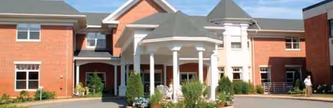 Brick senior living building with a white porte-cochere entrance and landscaped circular driveway.