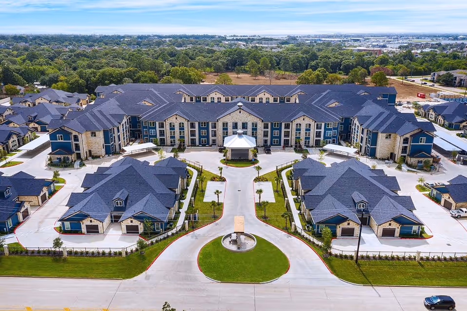 Aerial view of Chesapeake Bay - Luxury Active-Adult Community showing a large multi-building residential complex with blue and beige exterior, surrounded by greenery and parking areas.
