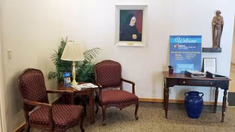 Two red chairs with a lamp and potted plant beside a desk in a small lobby.