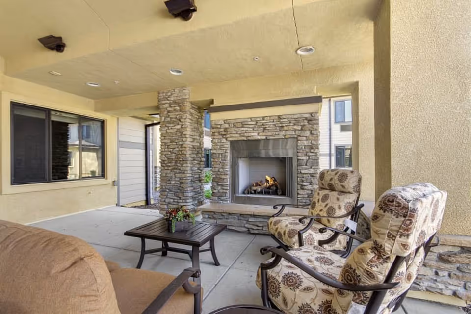 Covered outdoor patio with cushioned chairs, a coffee table, and a stone fireplace.