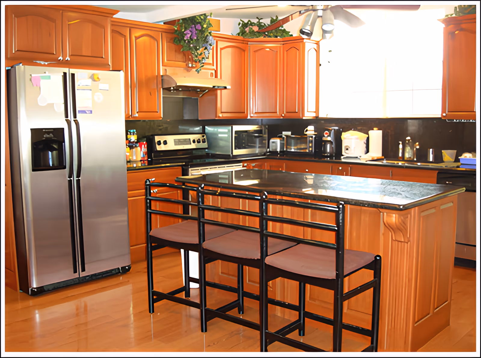 Bright kitchen with wooden cabinets, a center island with three bar stools, and a stainless steel refrigerator.