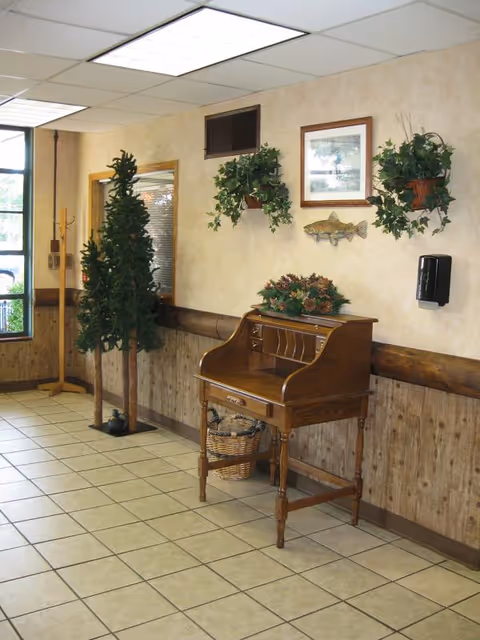 Entrance/lobby interior with a tiled floor, a wooden roll-top desk, potted plants, and wall decorations.