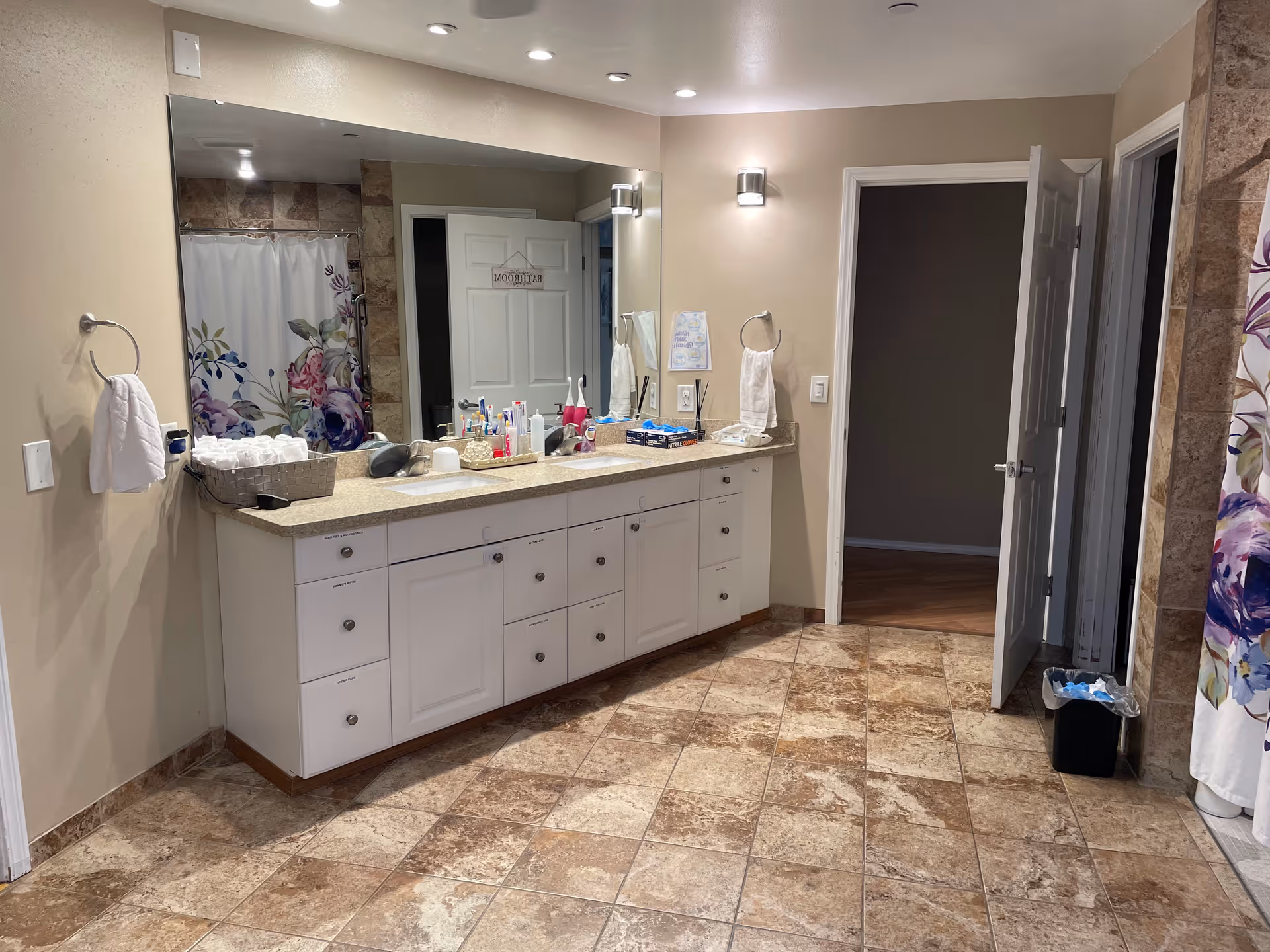 Spacious tiled bathroom with a long double-sink vanity, large mirror, and a floral shower curtain.