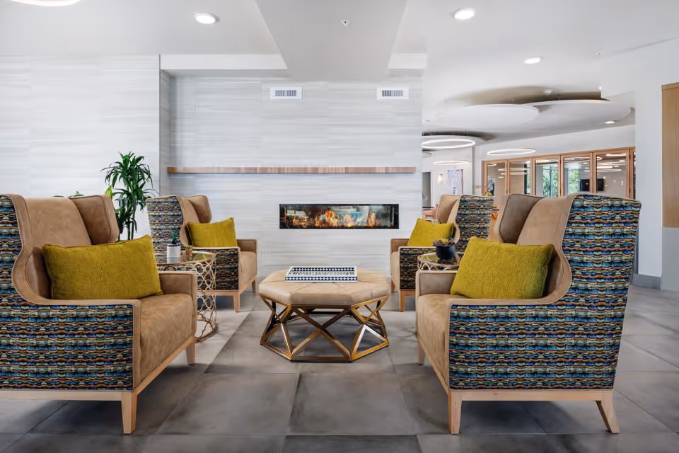 Modern seating area with patterned armchairs and green pillows arranged around an ottoman in front of a linear fireplace.