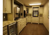 Small kitchenette with beige cabinets, granite countertops, sink, appliances and overhead lighting.