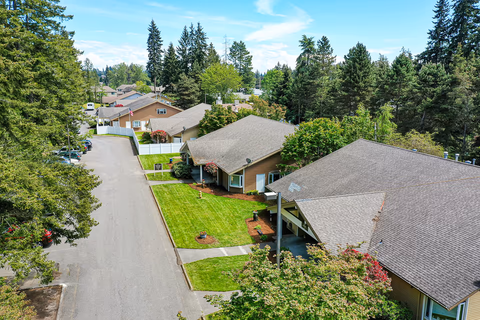 Aerial view of single-story cottage buildings with manicured lawns and a tree-lined street.