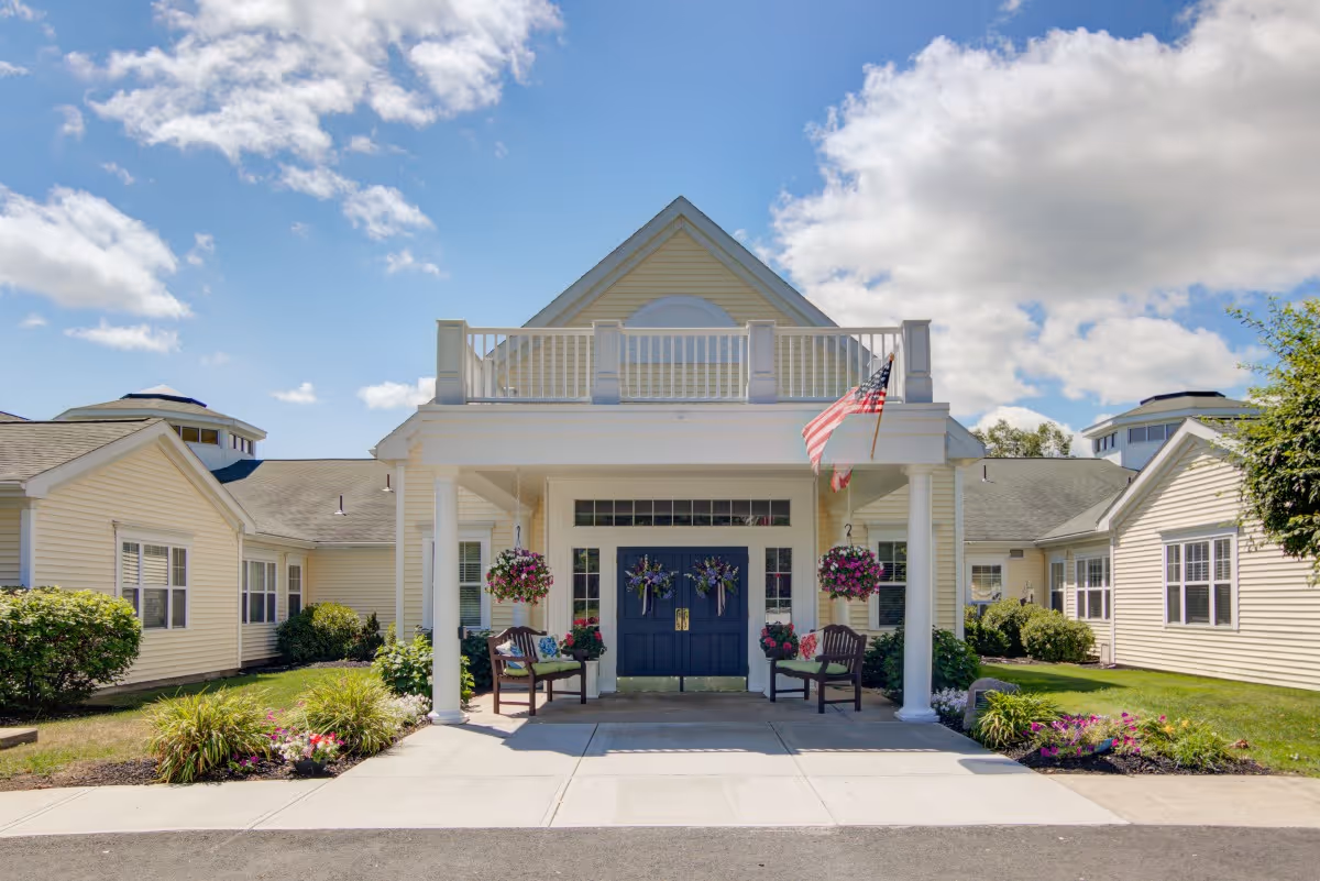 Front view of a light yellow senior living facility with a blue door and hanging baskets.