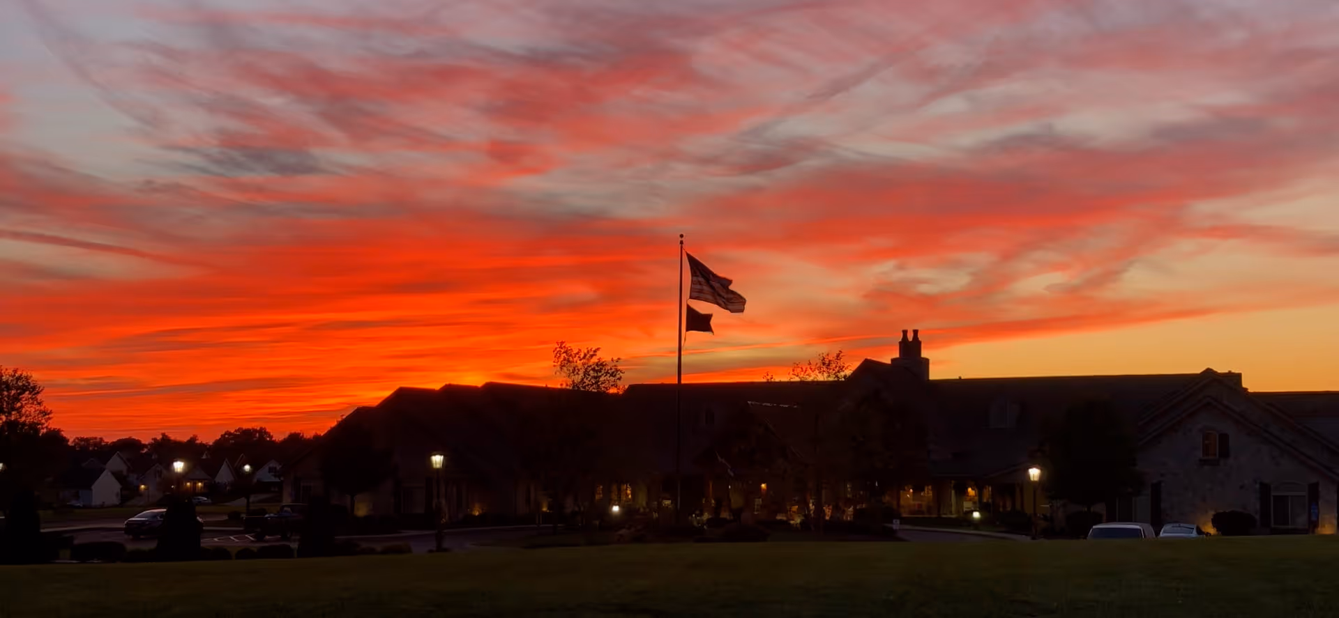 Silhouetted senior living building and flagpole set against a dramatic red-orange sunset sky.