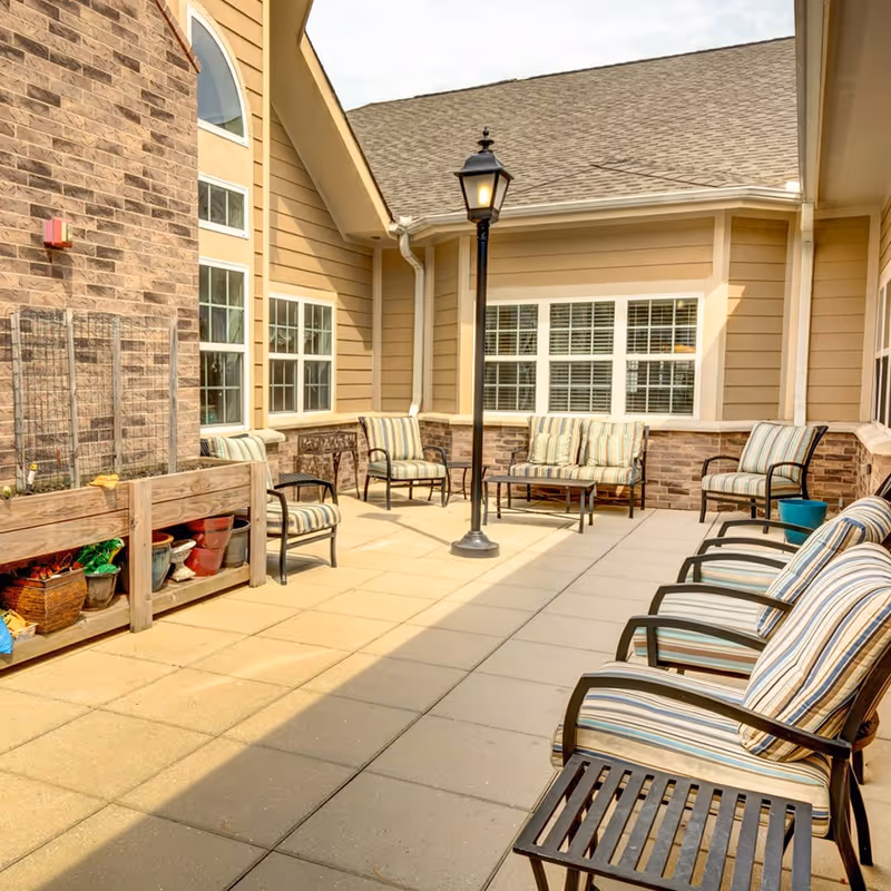 Outdoor patio with striped cushioned chairs around a central lamp post near a beige building.