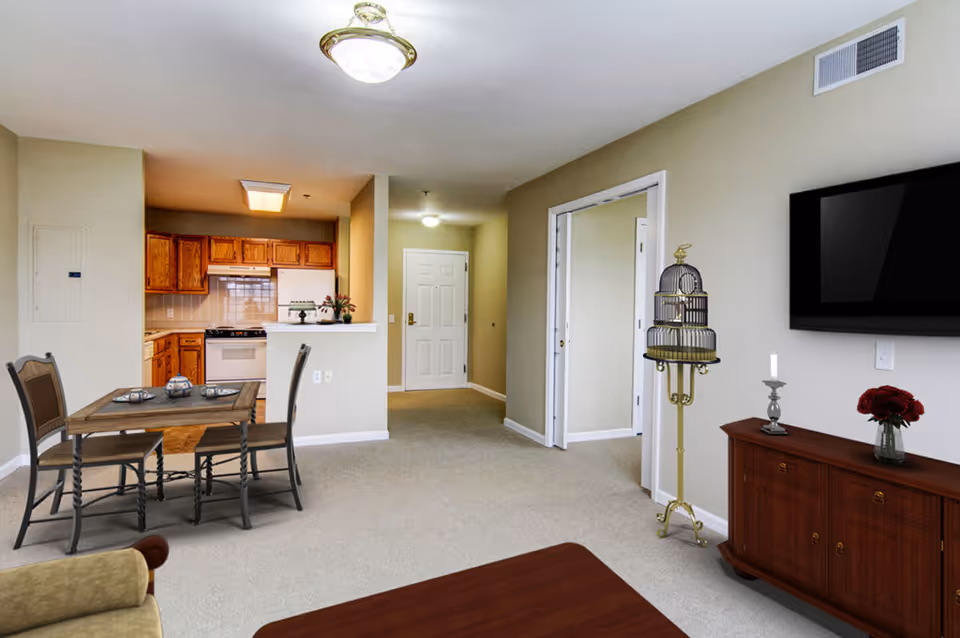 Open-concept living area with a dining table, kitchen in the background, a wall-mounted TV, and an entry door.