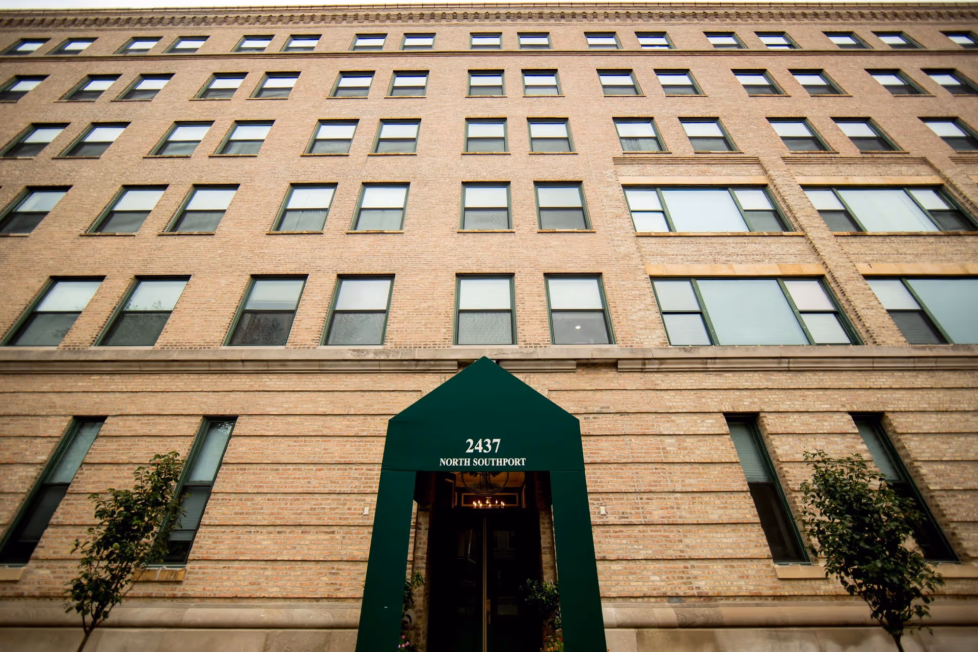 Exterior front view of a multi-story brick building with many windows and a green awning above the entrance displaying the address 2437 North Southport.