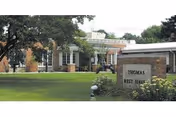 Exterior view of Thomas Rest Haven facility showing a brick building with large windows, surrounded by green lawn and trees. A sign in front reads 'Thomas Rest Haven'.