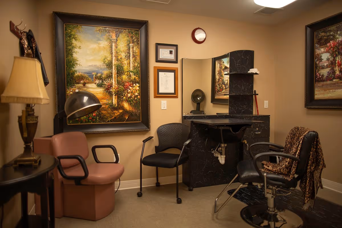 Small hair salon room with styling chairs, a wash sink and mirror, decorative lamps and large framed paintings on the walls.