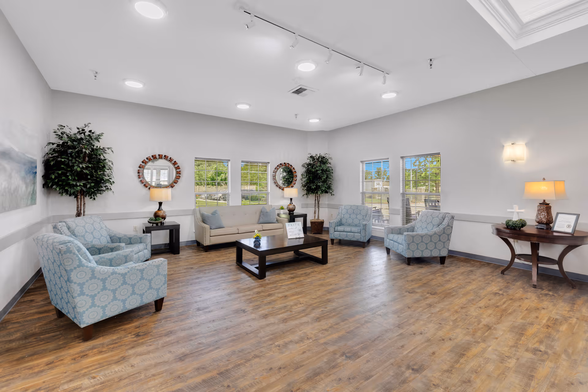 Bright, spacious lounge with a sofa, several patterned armchairs, coffee table, lamps, plants, and large windows.