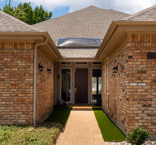 Brick building entrance with a gravel path leading to glass doors framed by brick walls.