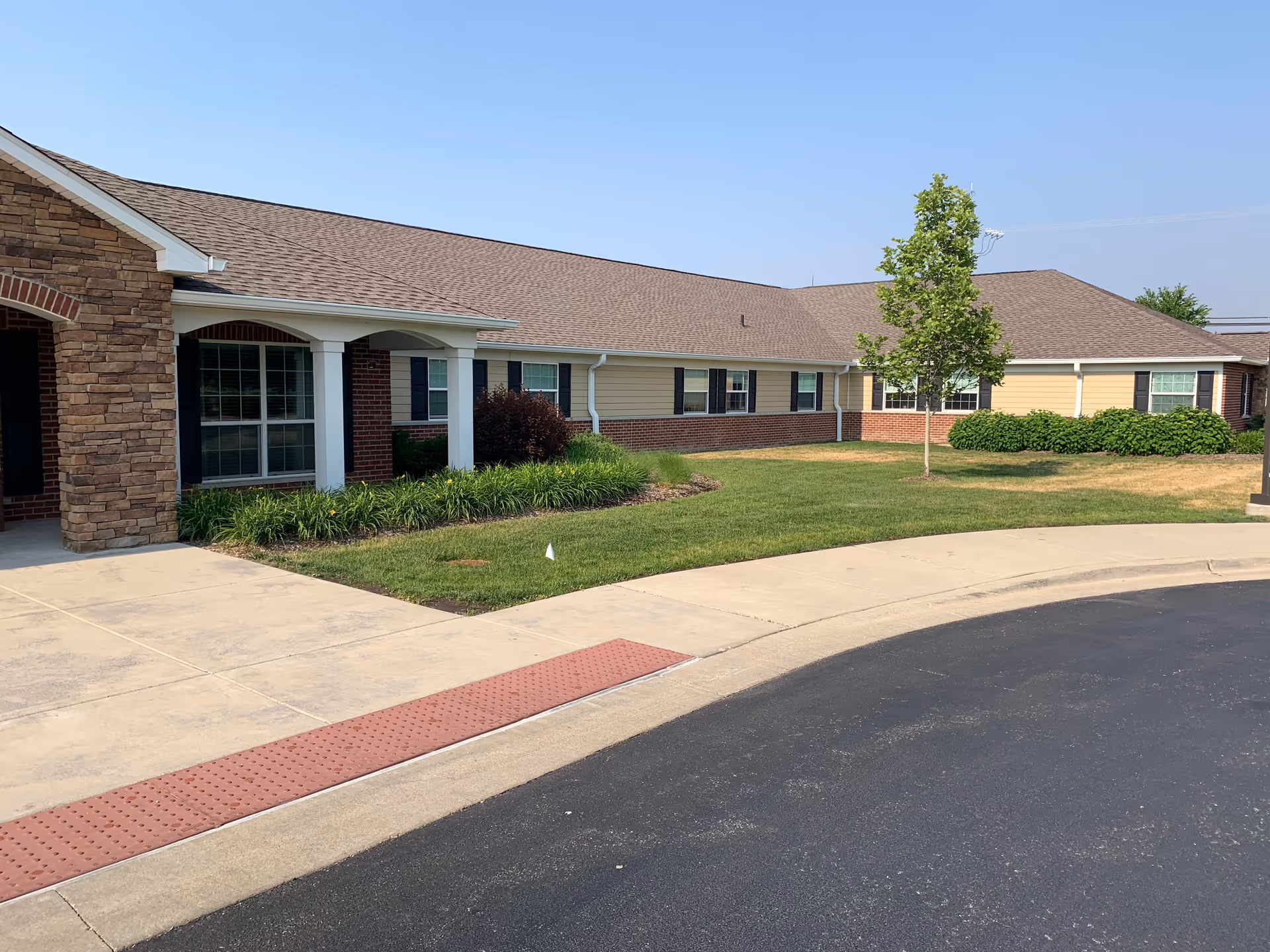 Single-story senior living facility exterior with brick detailing, landscaped lawn, and curved driveway.