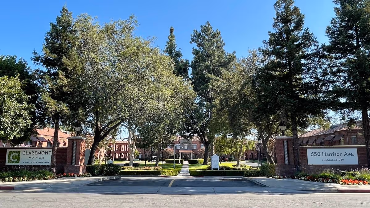 Front entrance and landscaped courtyard of Claremont Manor Retirement Community with trees, walkway, and brick signage reading 650 Harrison Ave.