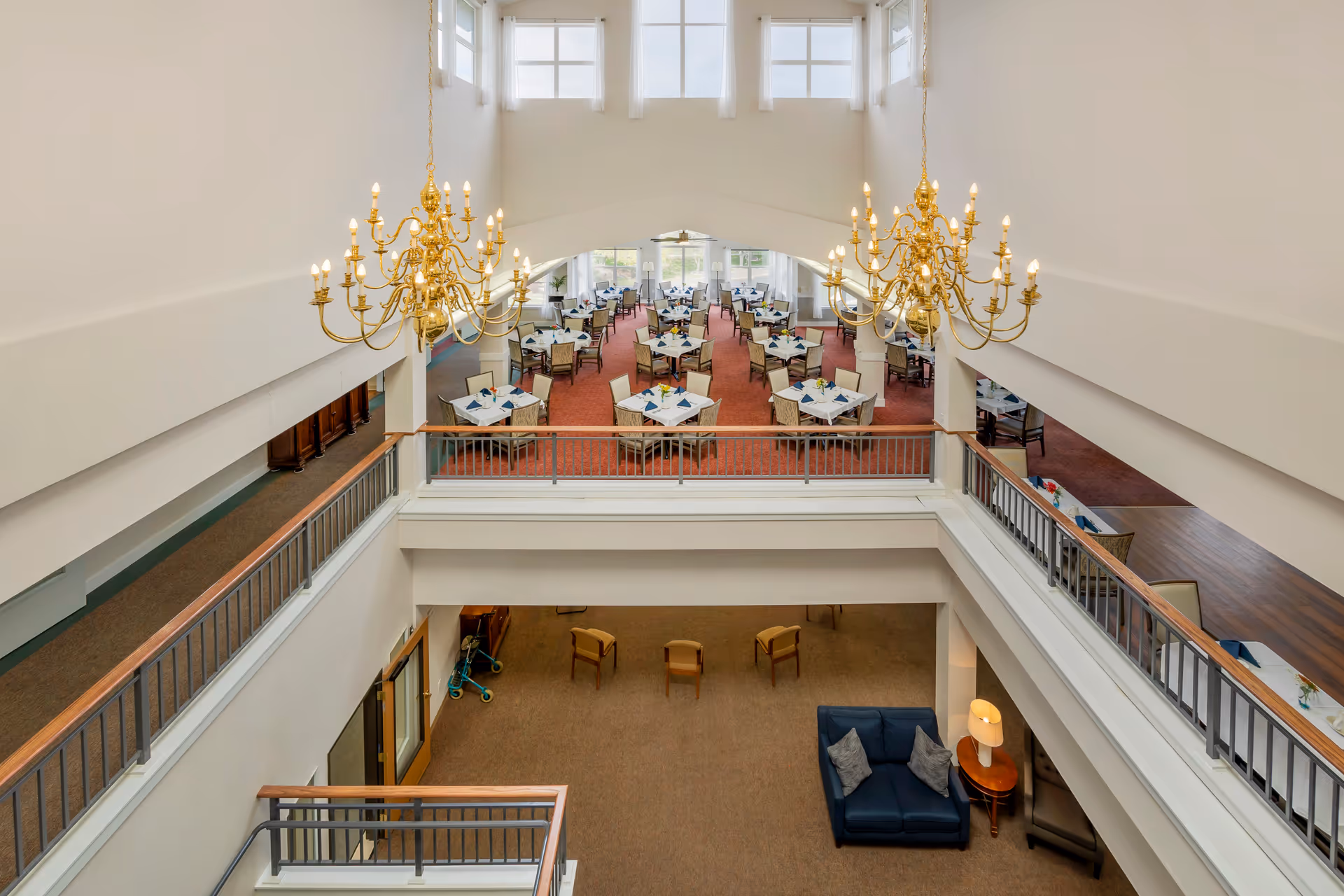 Spacious two-story dining area with gold chandeliers, multiple round tables set for meals, and a lower-level seating lounge.