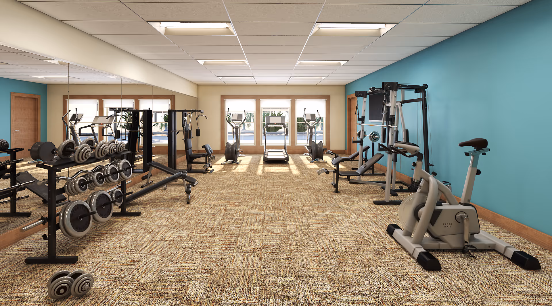 A fitness room with various exercise equipment including stationary bikes, weight machines, dumbbells, and treadmills. The room has a carpeted floor, teal and beige walls, large windows letting in natural light, and a large mirror on one side.