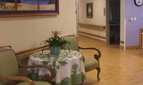 A seating area with a round table, potted plant, and patterned tablecloth in a hallway.