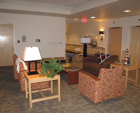 Furnished indoor lounge area with armchairs, a sofa, side tables, lamps and plants in a hallway/common space.