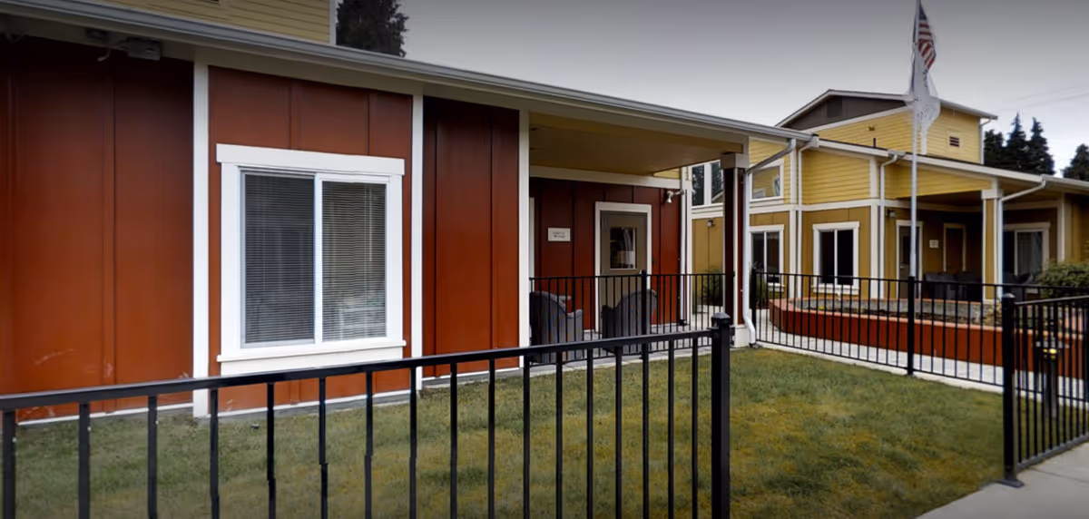 Colorful cottage-style senior living buildings in Marysville with a black fence and small grassy lawn.