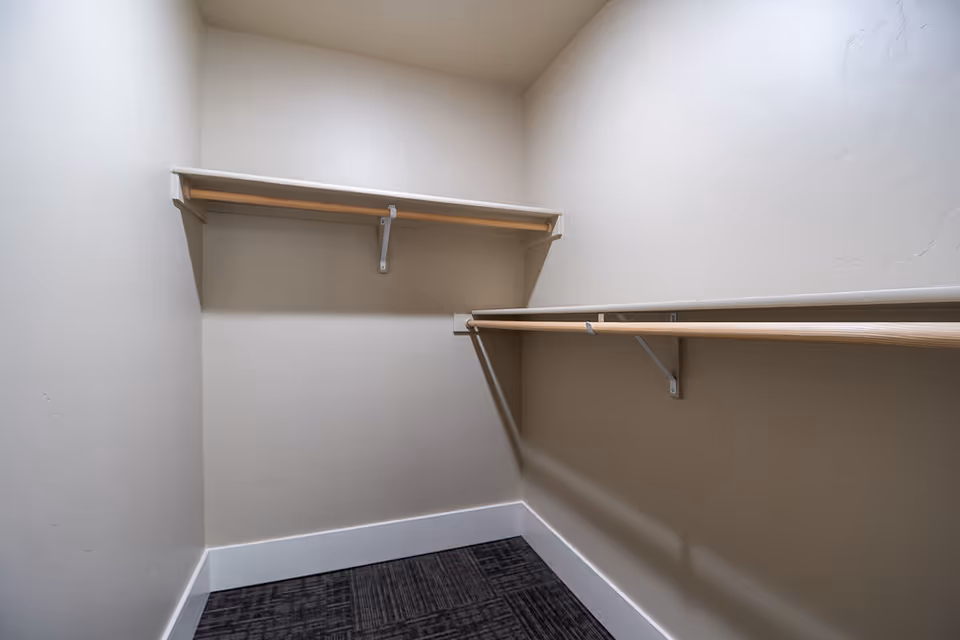 Empty walk-in closet with beige walls, carpeted floor, and wooden hanging rods on two sides.