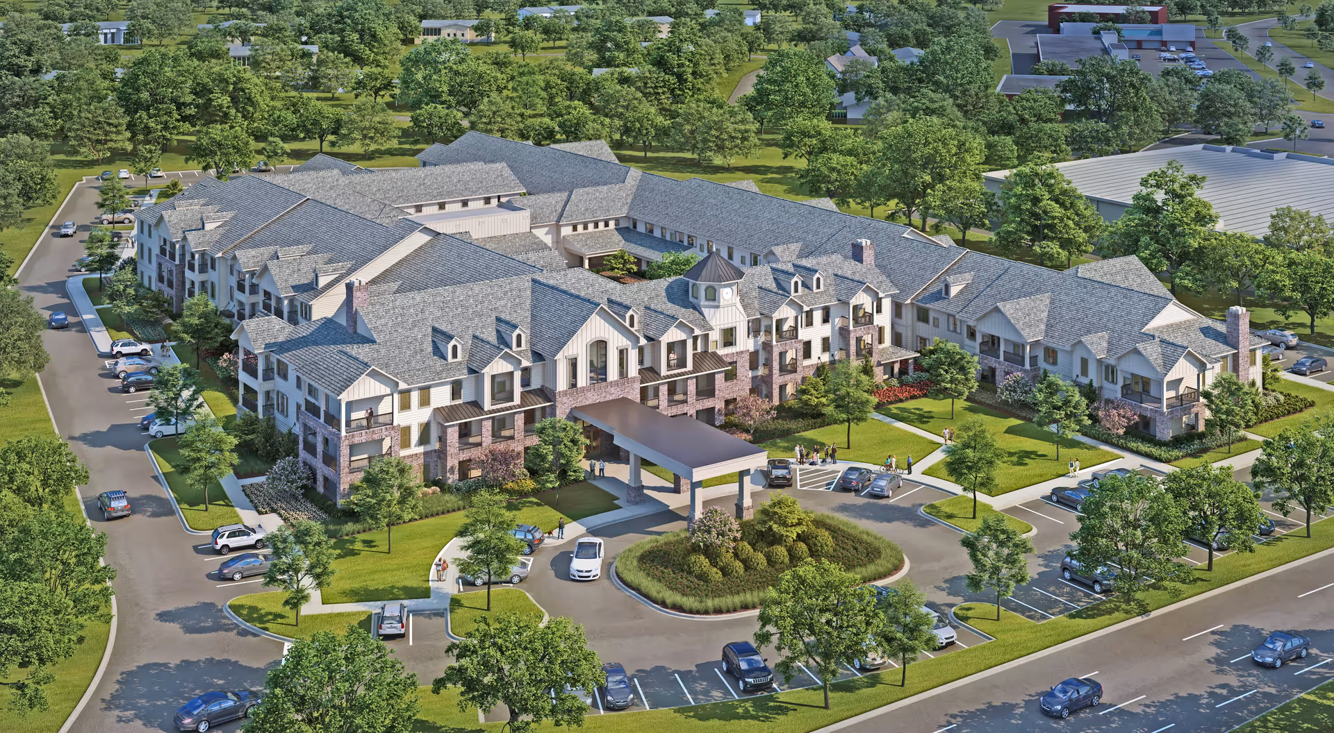 Aerial view of Harper's Station Yorktown, a large senior living facility with multiple connected buildings featuring gray roofs and white exterior walls with brick accents. The facility is surrounded by green lawns, trees, parking lots with cars, and walkways. Several people are visible near the entrance and around the grounds.