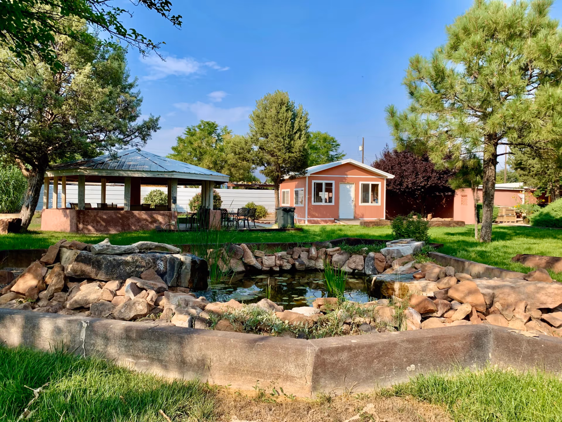 Outdoor courtyard with a pond and rock garden in front of a pavilion and a small pink building.