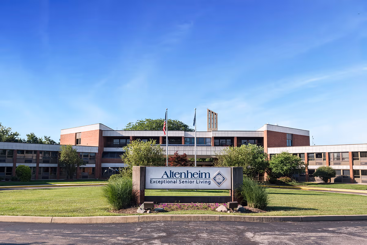 Front exterior of the Altenheim senior living facility with a lawn and entrance sign under a blue sky.