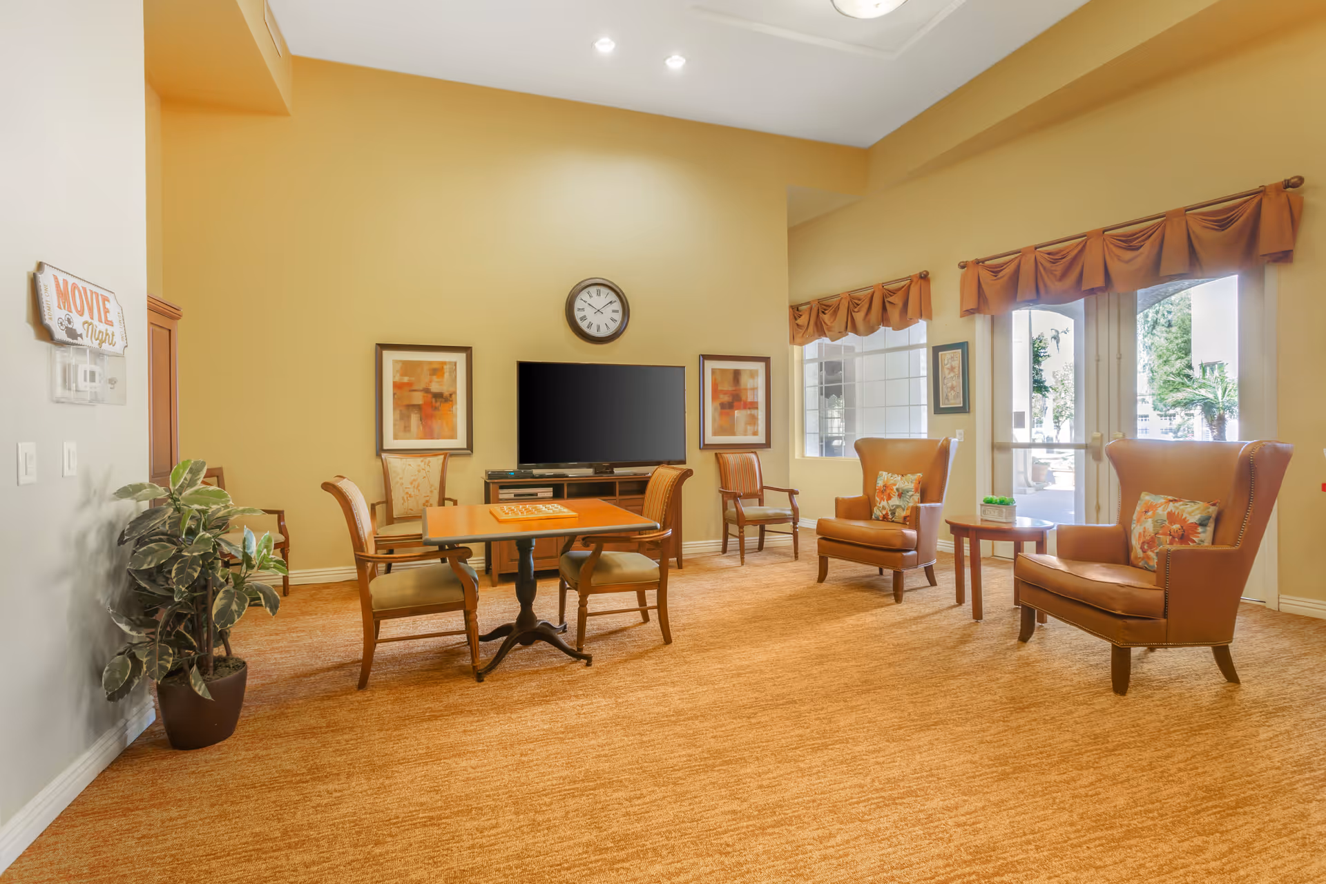 Bright common lounge with armchairs, a small game table, side tables, and a wall TV.