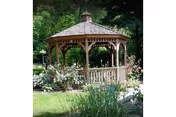 A wooden gazebo surrounded by greenery, flowering shrubs, and a grassy lawn in a garden.