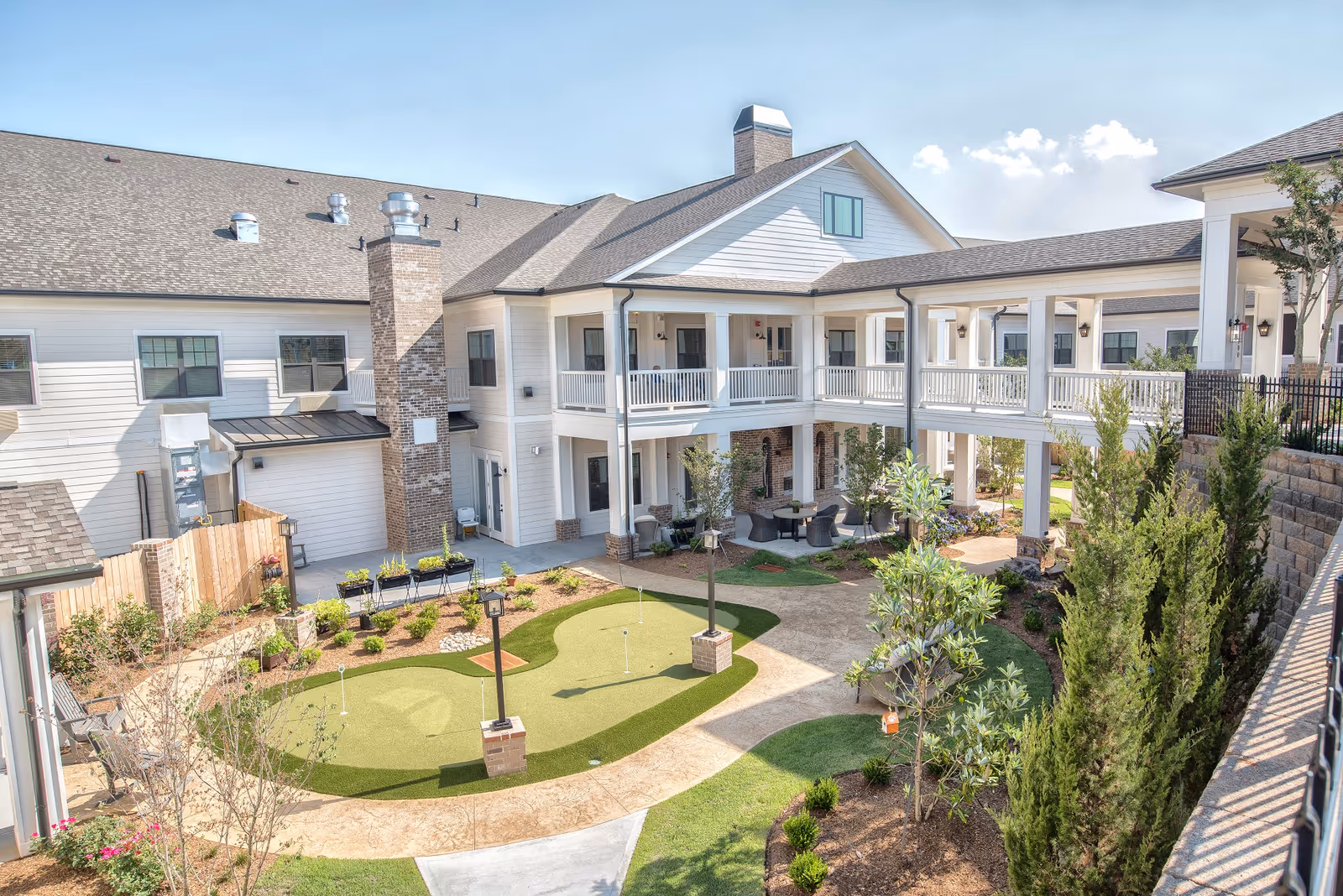 Sunny central courtyard of a two-story senior living complex featuring a small putting green, landscaped paths, and covered balconies.