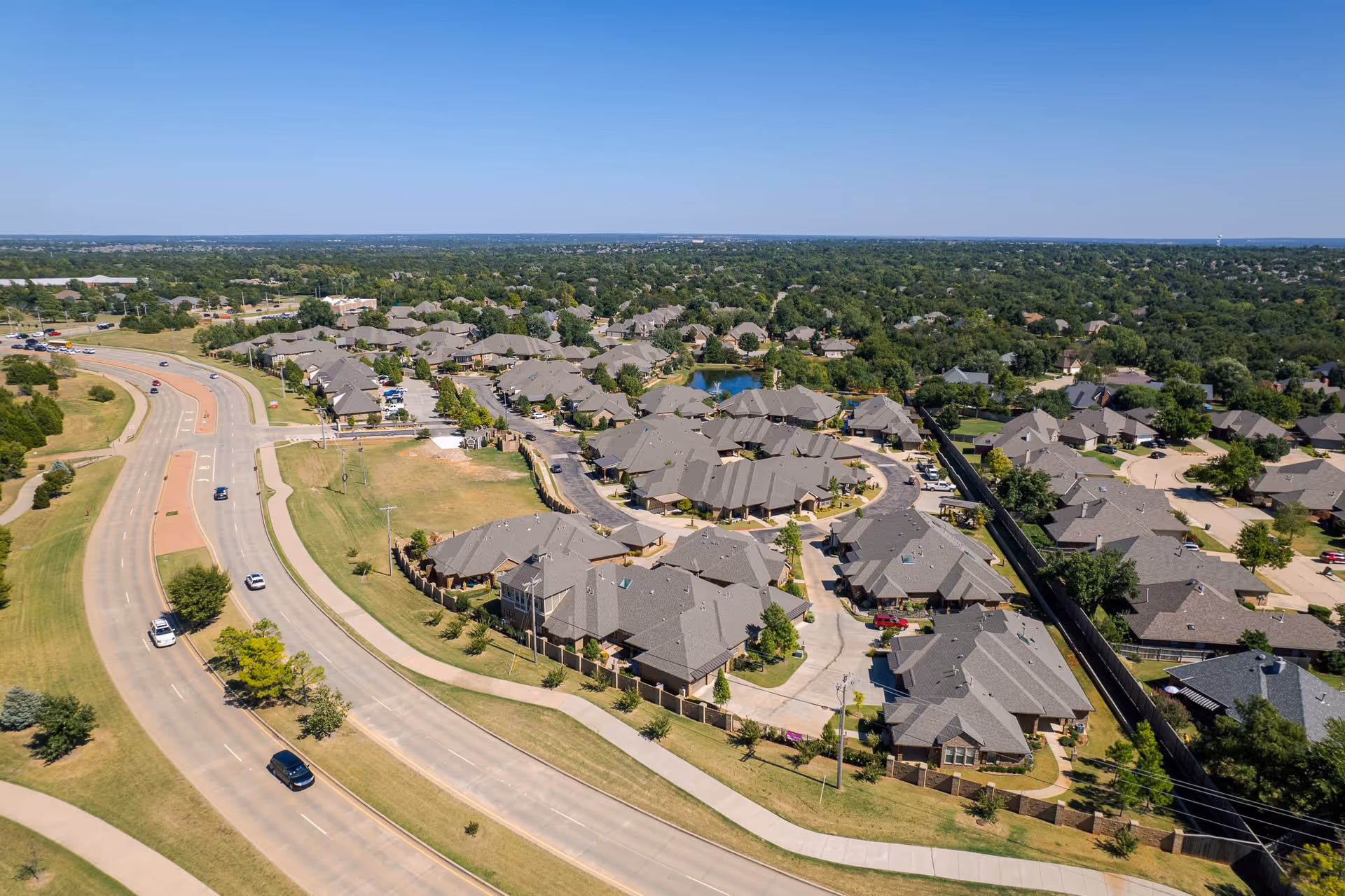 Aerial view of a residential neighborhood with multiple houses, roads, and green spaces under a clear blue sky.
