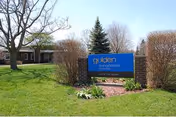 Outdoor view of the Golden LivingCenter - Mishawaka sign on a grassy area with trees and bushes around, and a building visible in the background under a clear sky.