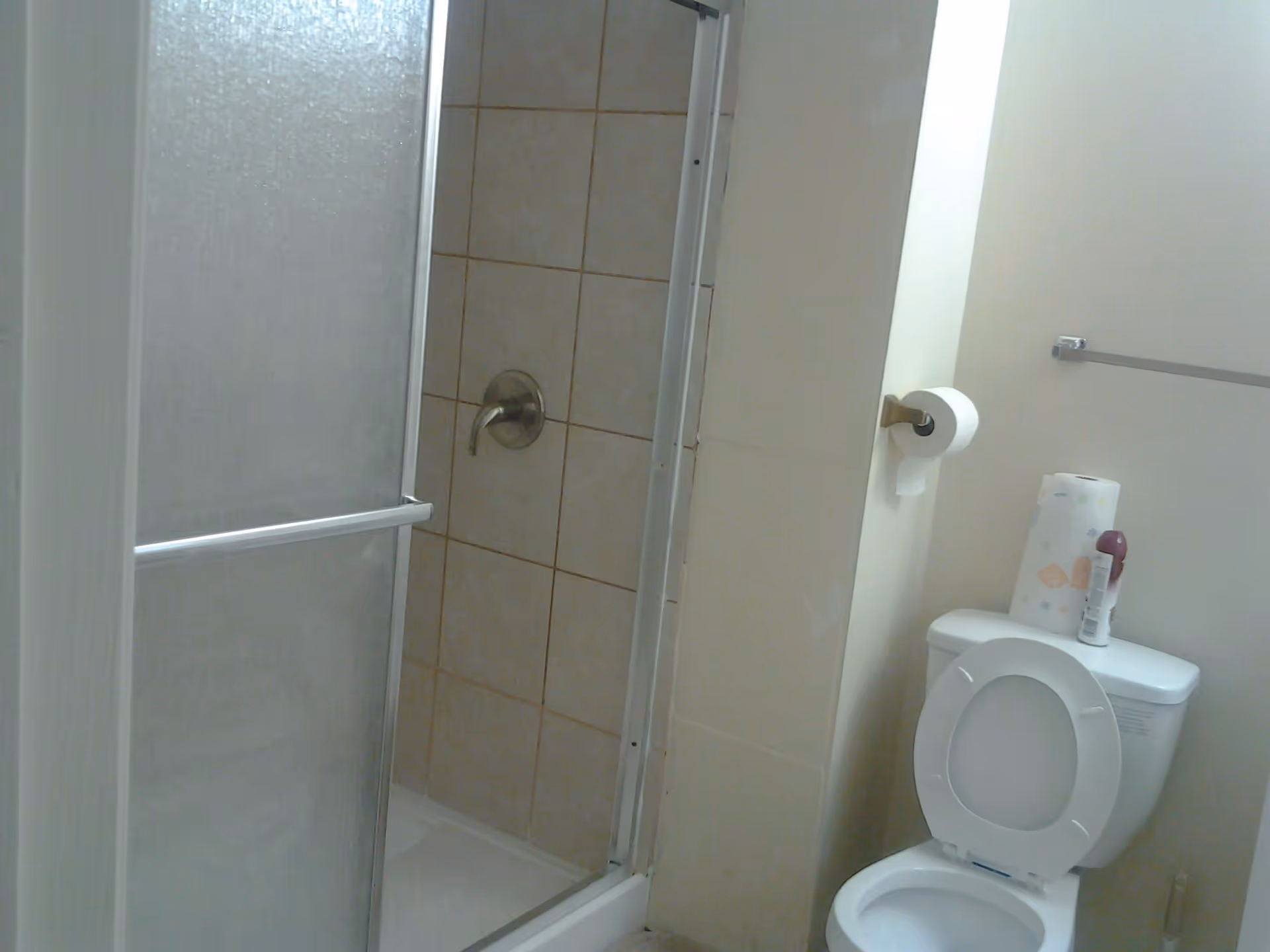 Small bathroom showing a tiled shower with a sliding glass door and a toilet with the lid up and a roll of toilet paper on the wall.