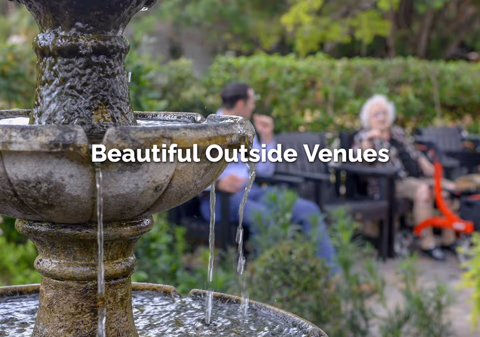 A close-up stone fountain with flowing water in a garden, with blurred benches and people in the background and the text "Beautiful Outside Venues" overlaid.
