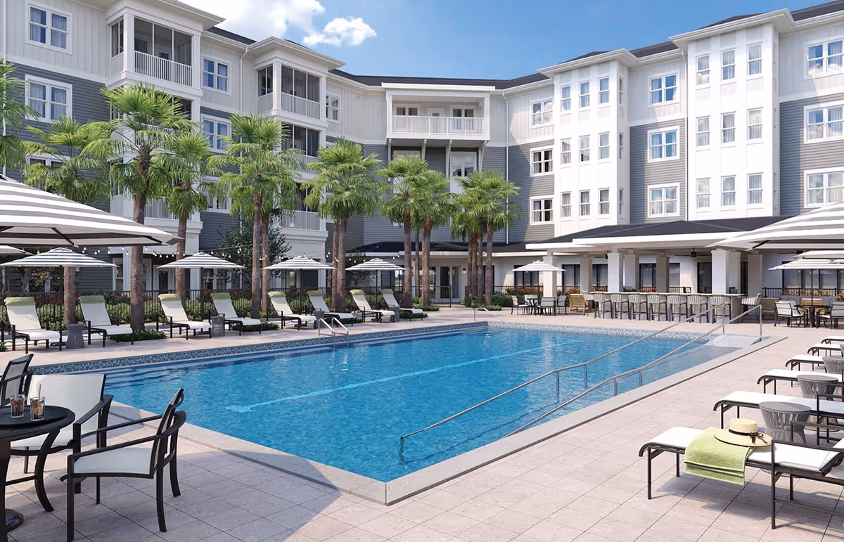 Outdoor swimming pool surrounded by lounge chairs, umbrellas, palm trees and a multi-story residential building.