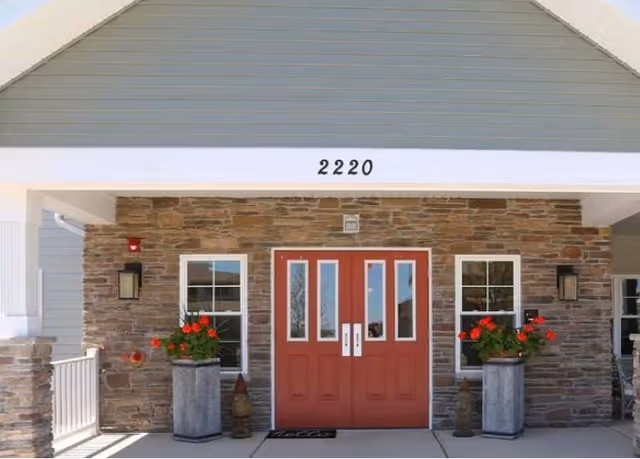 Front entrance with red double doors, stone facade, potted flowers, and the number 2220 above the doorway.